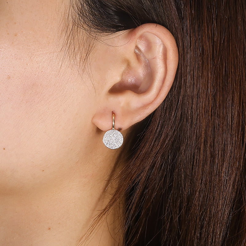 A gold tone round gem encrusted drop earring being worn.