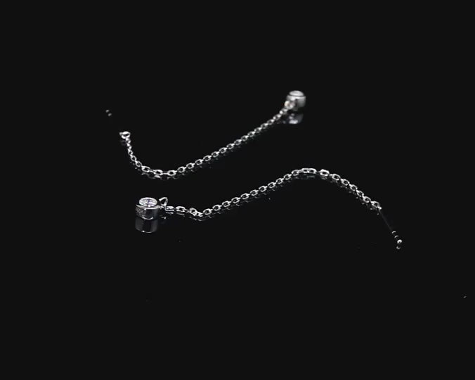 A silver pair of chain dangle earrings bezel set with moissanite spinning on a viewing platform.