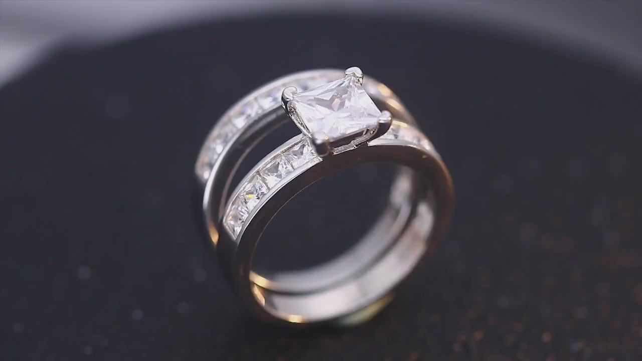 A silver ring set with small princess cut zircons, channel set in the shank and a princess cut moissanite set as the main gem. This ring is paired with a matching wedding band. Both are spinning on a viewing platform.