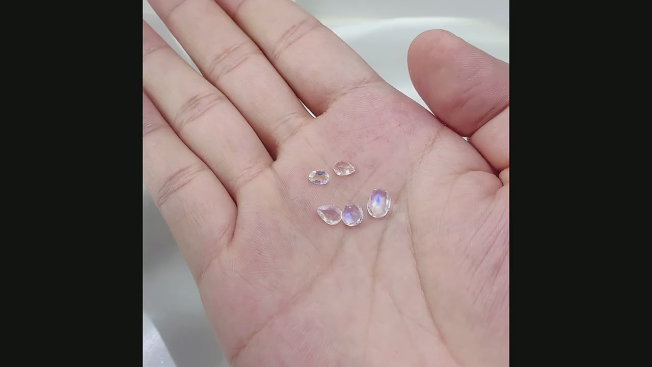 A hand displaying 5 sparkling tear drop cut blue moonstones.