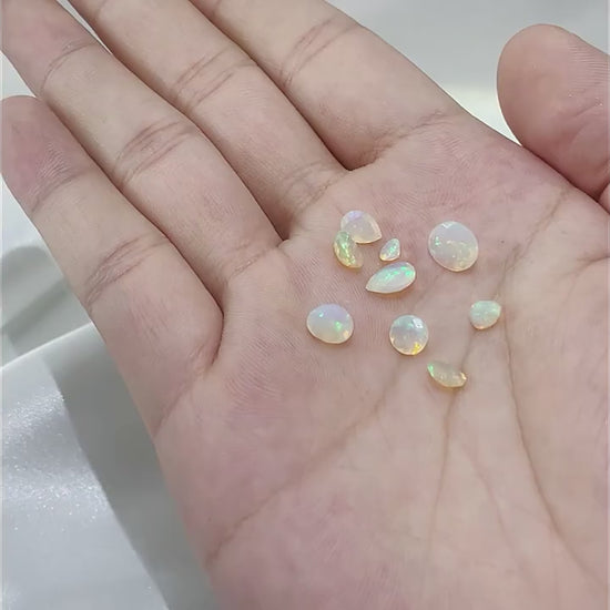 Various sizes and shapes of loose colorful opals displayed in a hand.