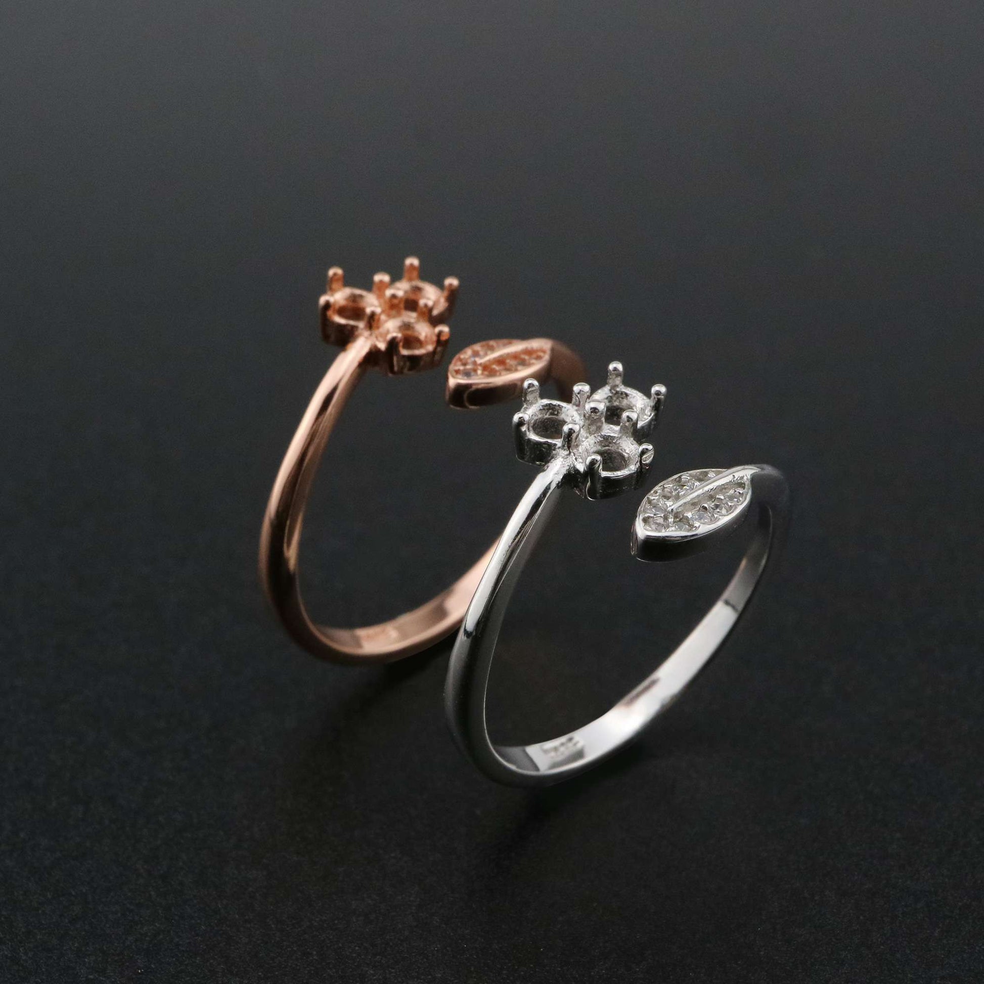 One silver and one rose gold bypass rings setting with a leaf on one side and a semi mount for three small round gems on the other.