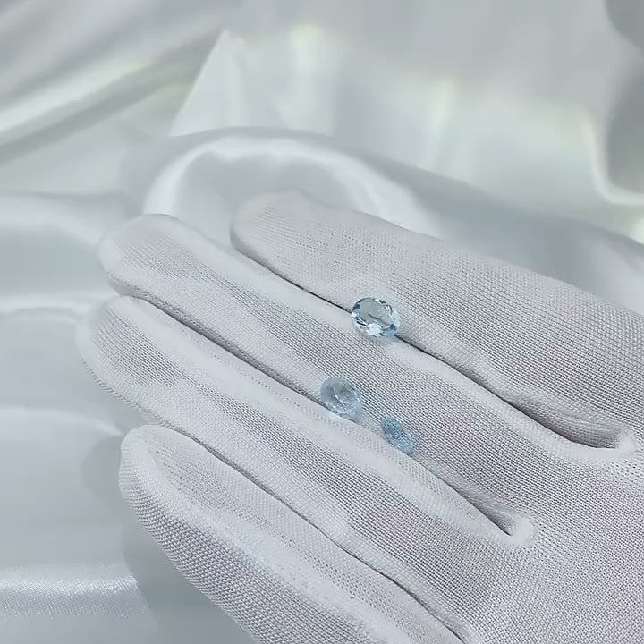 A hand holding and displaying 3 light blue oval aquamarine gems.