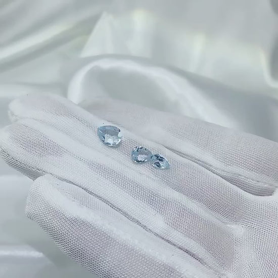 A hand holding and displaying 3 tear drop cut light blue aquamarine gems.