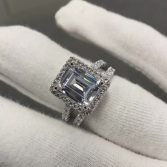 A silver engagement and wedding set with a  emerald cut halo ring and matching eternity band being displayed.