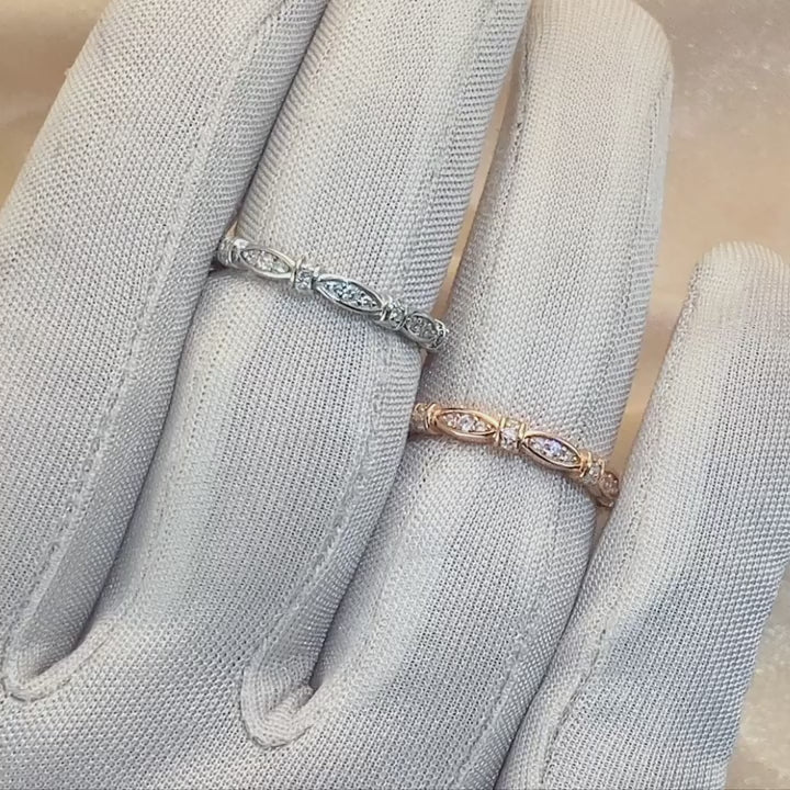 A hand wearing one silver and one rose gold ribbon scalloped style ring set with clear small gems, displaying them.
