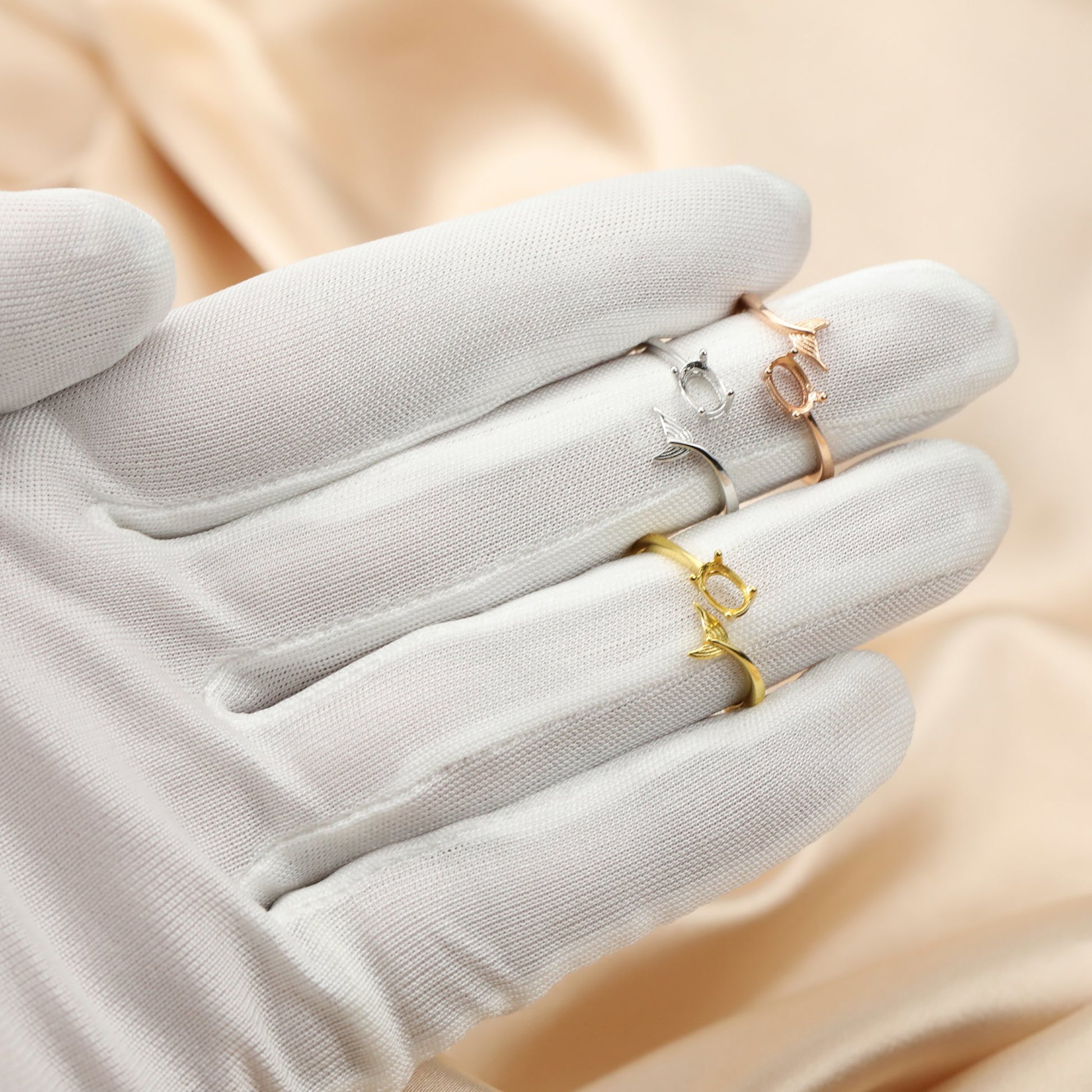 A hand wearing one silver, one gold and one rose gold oval wrap around rings with a mermaid tail on the opposite ends.