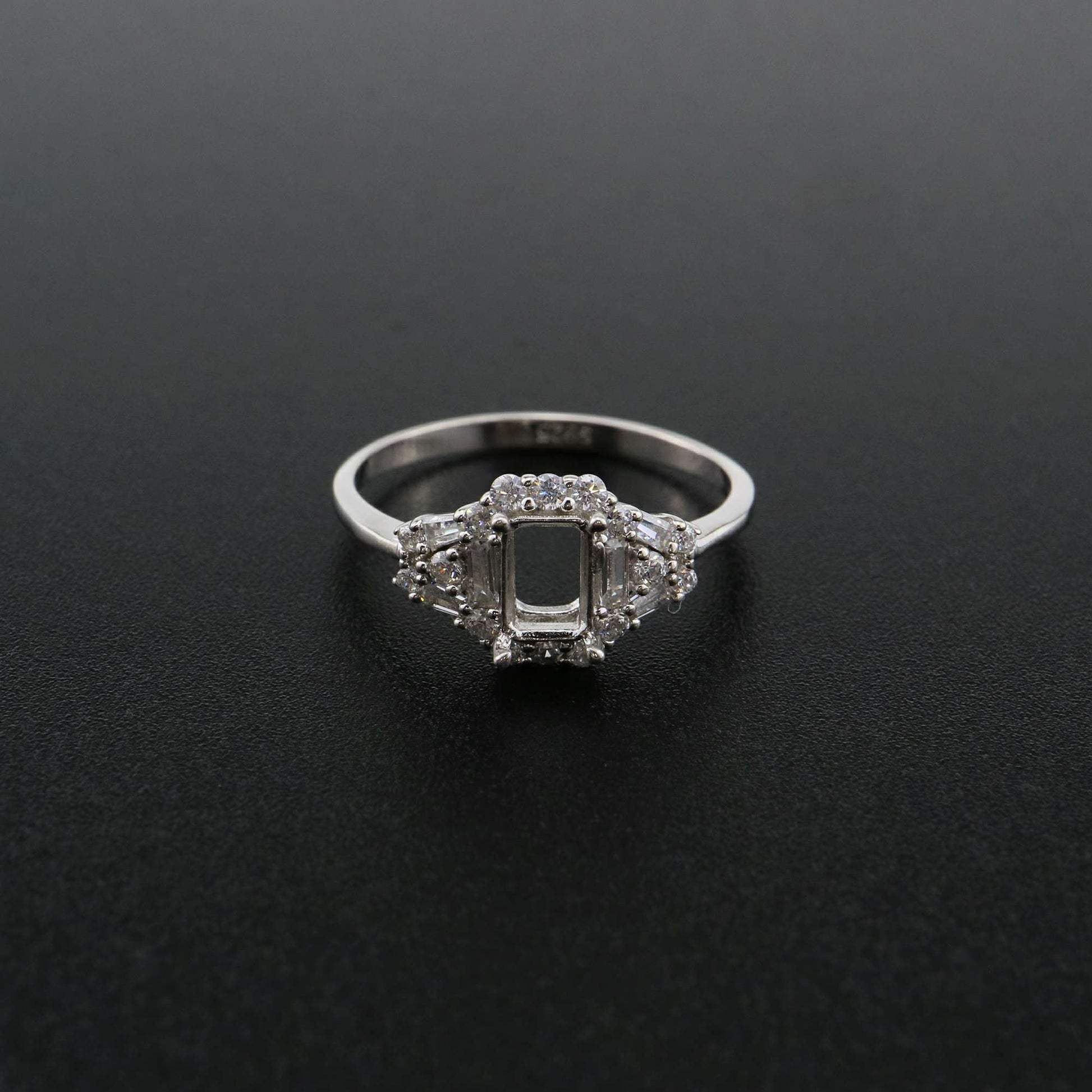 A silver emerald cut semi mount with a CZ halo of emerald and round cut gems.