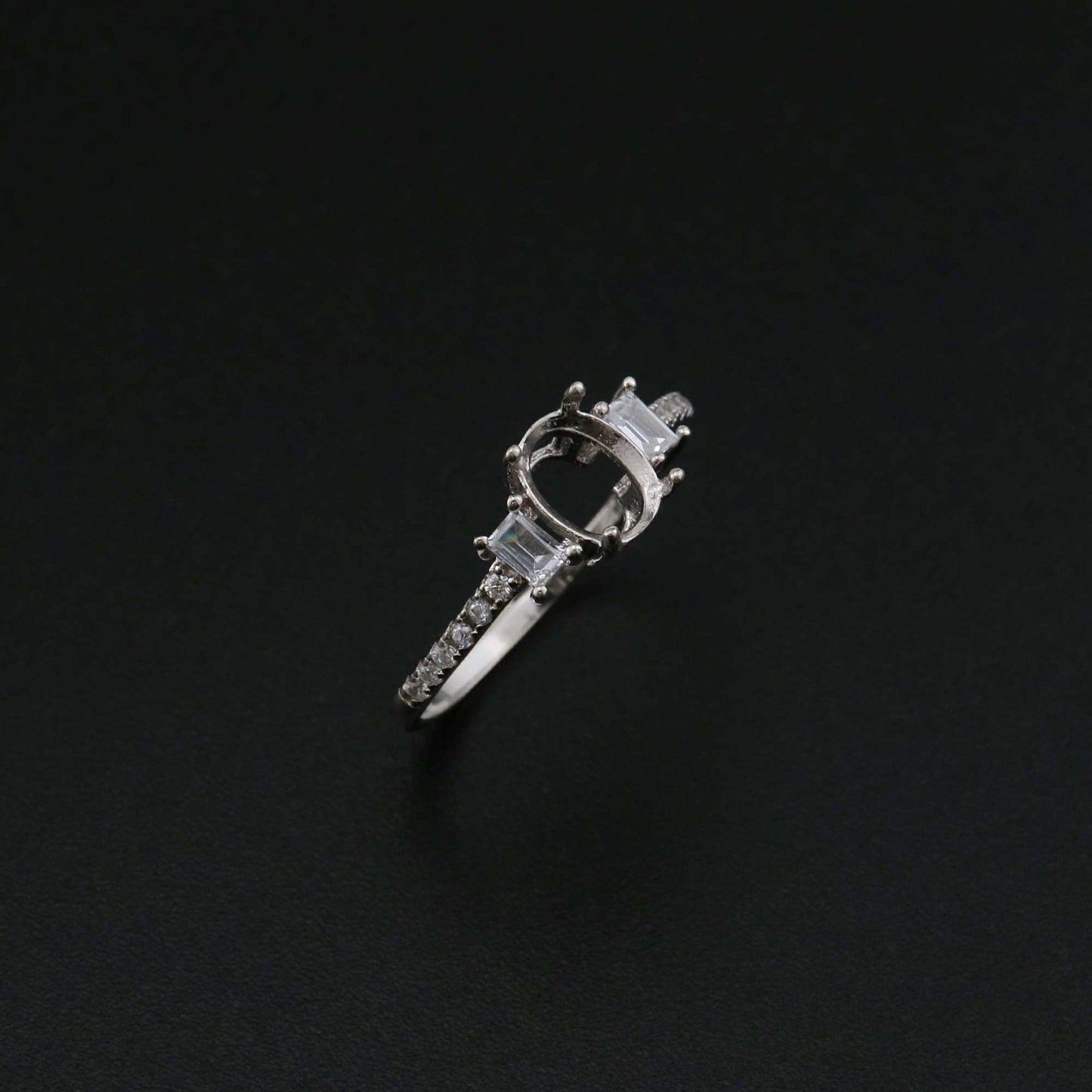 A silver oval shaped 3 stone semi mount with emerald cut gems on the sides.