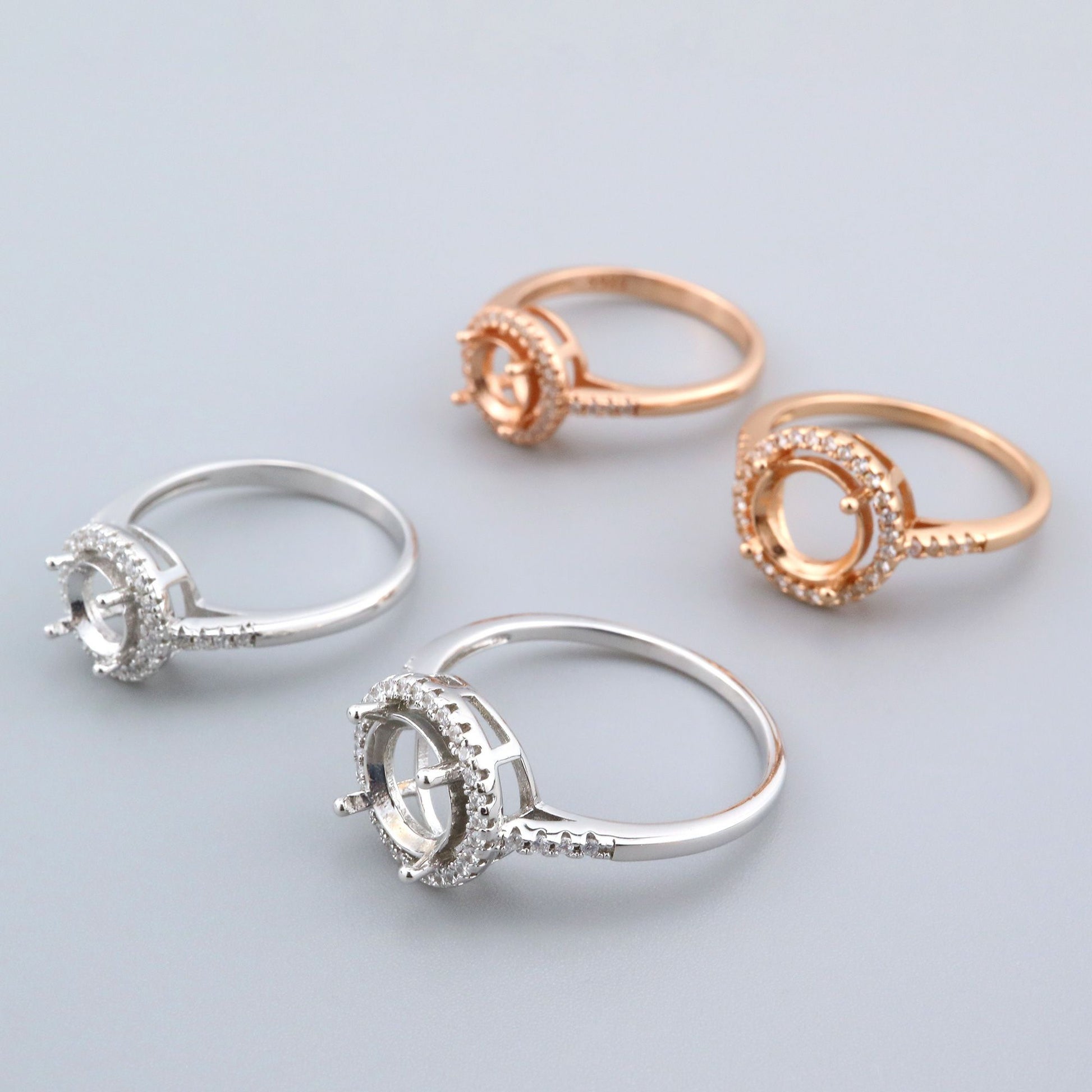 Two silver and two rose gold round halo semi mounts.