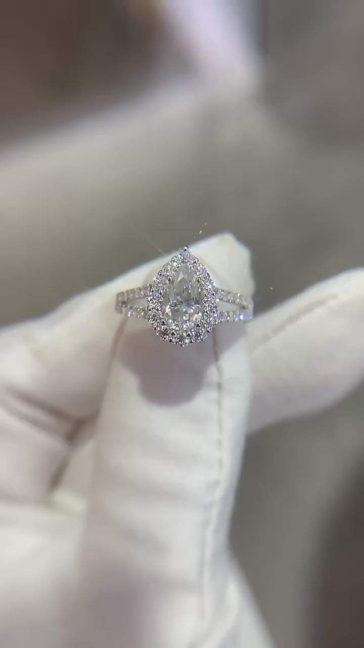 A hand displaying a silver tear drop halo split shank engagement ring.