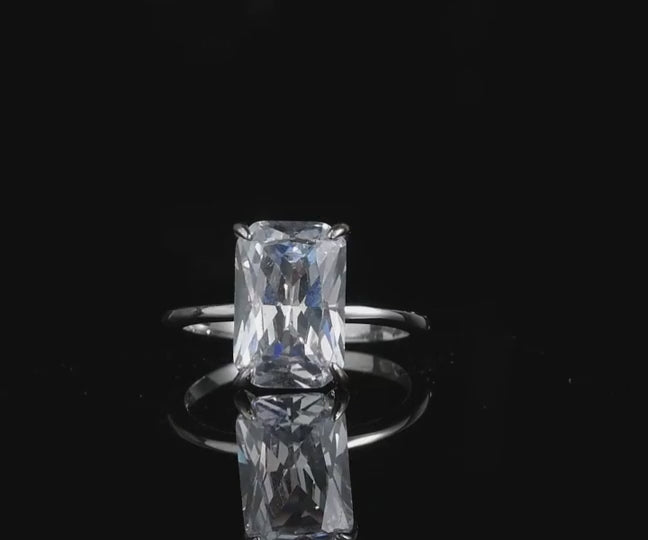 A silver large radiant cut solitaire engagement ring spinning on a platform.