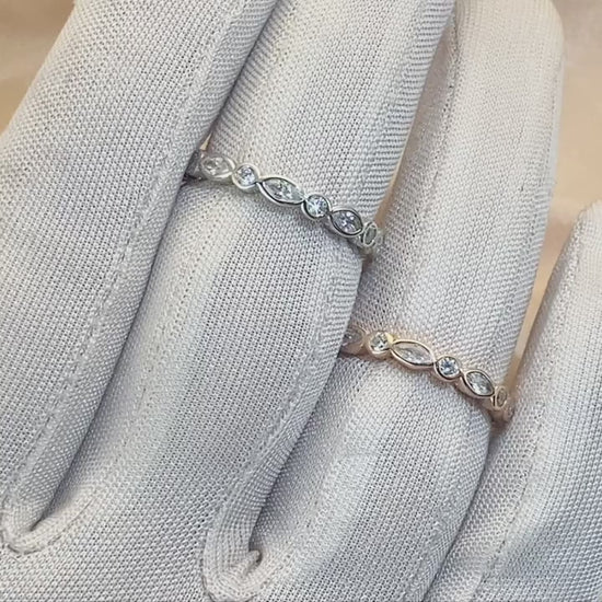 A hand wearing and displaying one silver and one rose gold ring bezel set with alternating marquise and round cut clear gems.