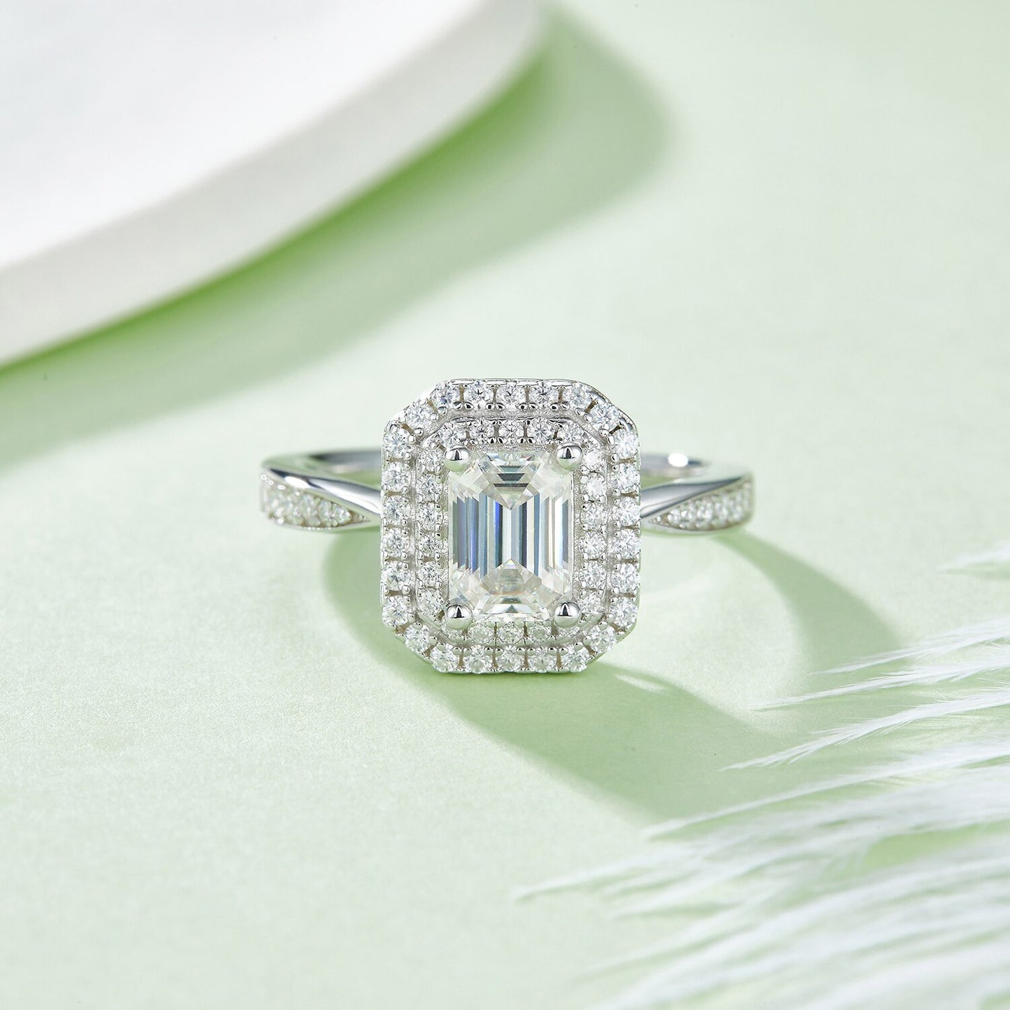 A silver ring set with an emerald cut moissanite in a double halo with a tapered gem encrusted band.