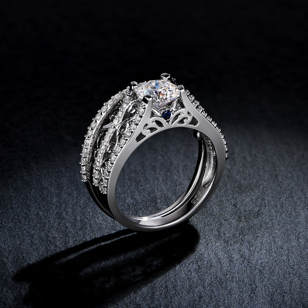 A filigree silver moissanite engagement ring with a small blue sapphire set on each side and a matching wedding band.