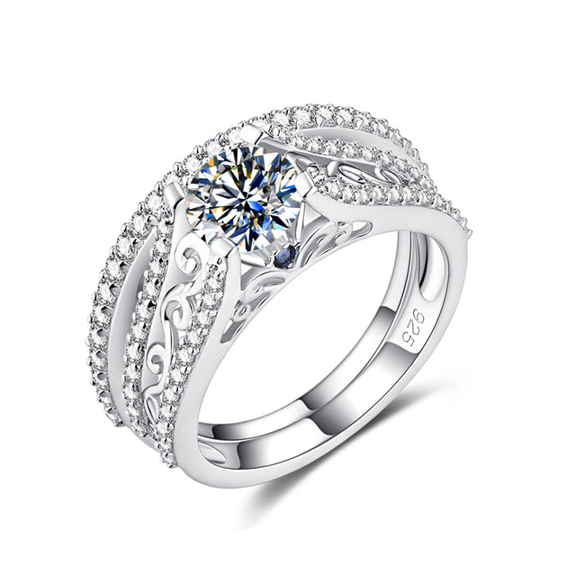 A filigree silver moissanite engagement ring with a small blue sapphire set on each side and a matching wedding band.