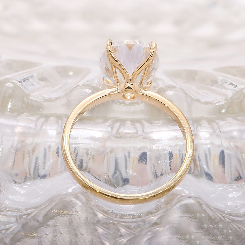 A gold band solitaire set with petal style prongs holding a 3CT oval moissanite.