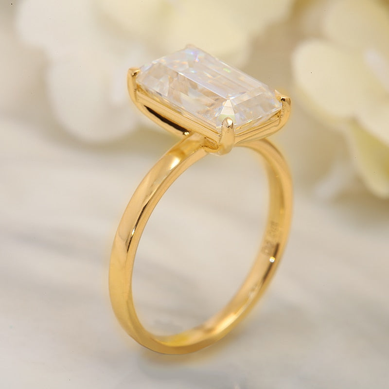 A gold solitaire ring basket set with a 4CT emerald cut moissanite.