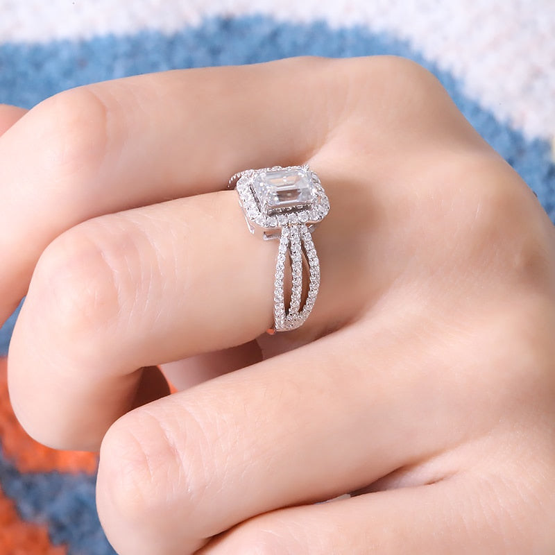 A hand wearing a silver emerald cut halo ring with a triple split pave band.