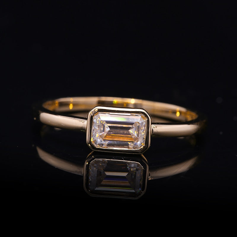 A silver ring that has a emerald cut moissanite bezel set east to west.