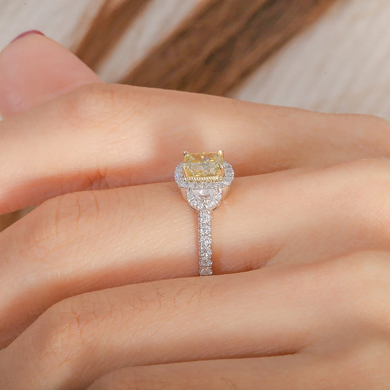 A hand wearing a silver halo ring set with a yellow moissanite and two crescent halo clear moissanites on each side.