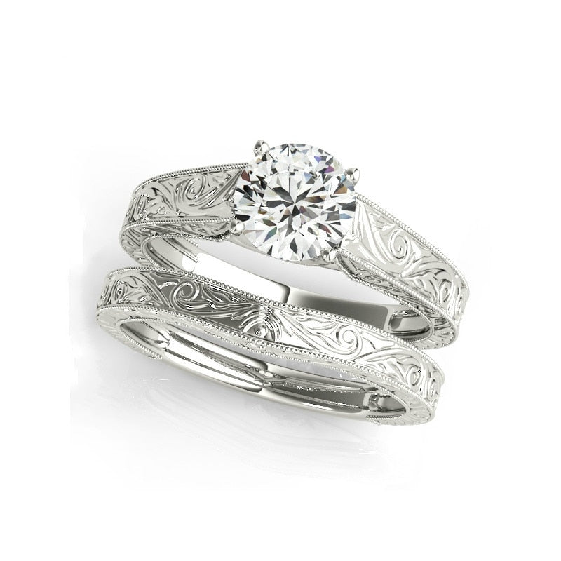 A silver embossed swirl design shank set with a round cut moissanite, accompanied by a matching wedding ring.
