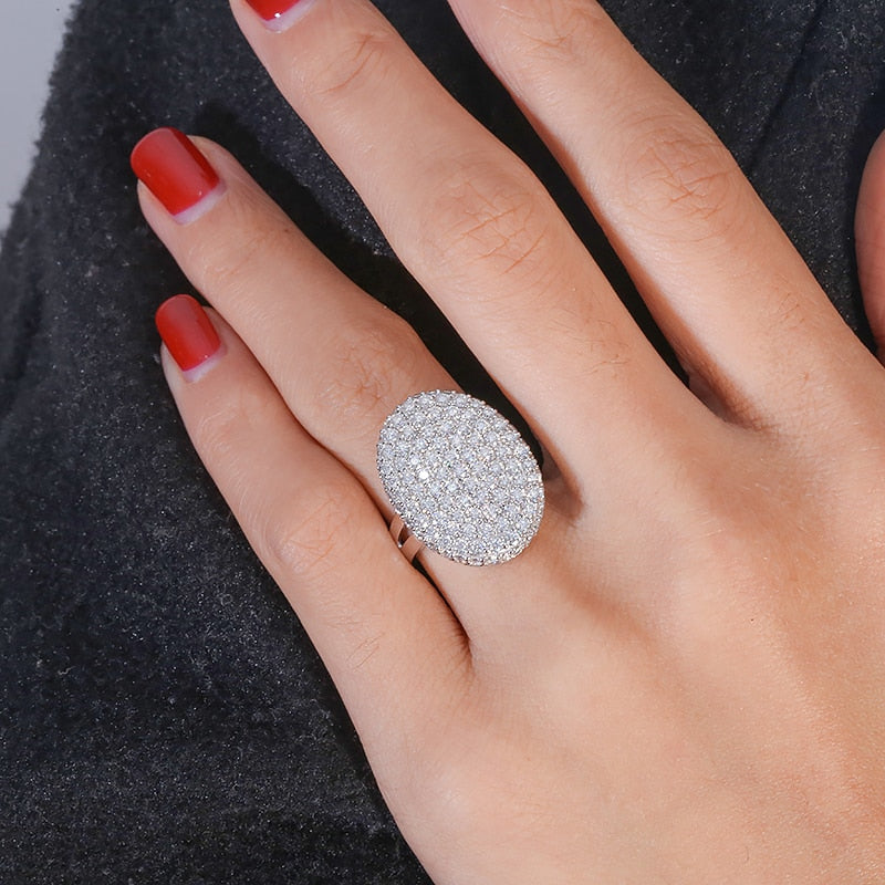 A hand wearing a oval shaped silver gem encrusted thick shield style ring.