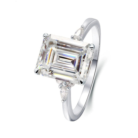 A silver ring with a 5CT emerald cut moissanite set between small round and small pear cut moissanites.