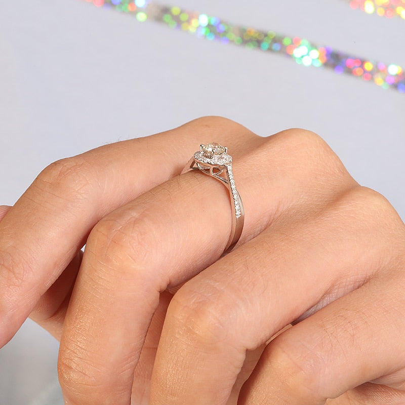 A hand wearing a silver round halo ring with a half pave split shank twisted band.