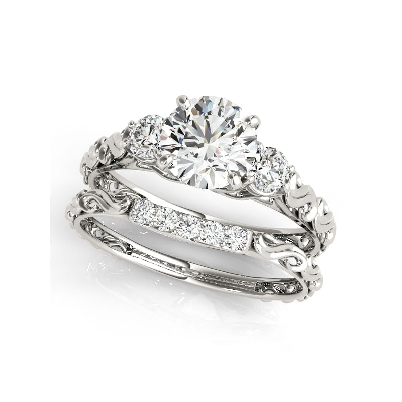 A silver filigree ring set with a 1CT moissanite and a smaller gem on each side; paired with a matching 5 gem wedding ring.