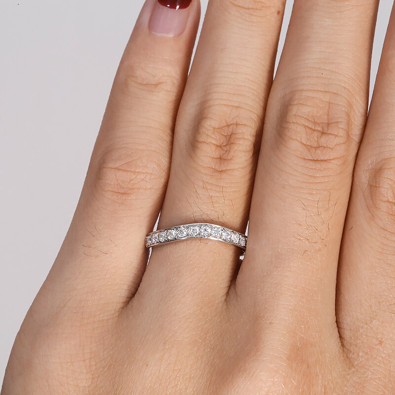 A hand wearing a silver curved wedding band with moissanites along the band.