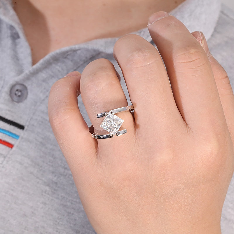 A hand wearing a silver ring bypass and tension set with a princess cut moissanite.