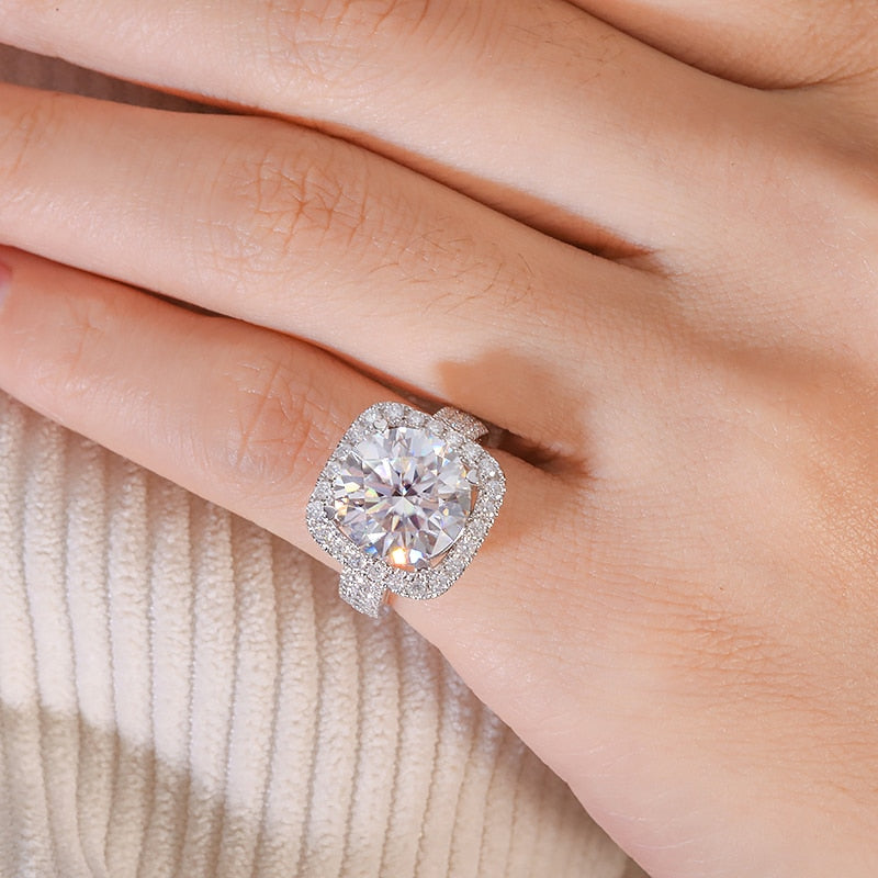 A hand wearing a silver halo ring set with a 8CT round moissanite in a wide half pave band.