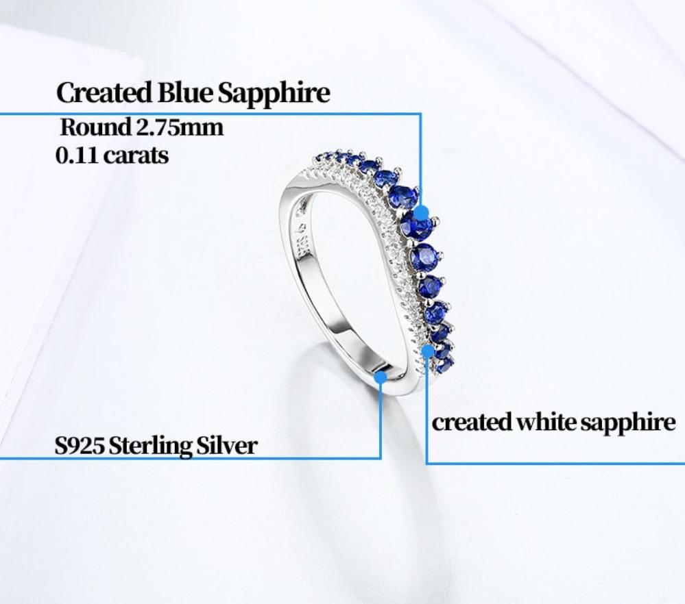 A silver wave design band with varying size blue sapphires and small clear gems below the sapphires.