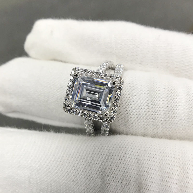 A silver engagement and wedding set with a  emerald cut halo ring and matching eternity band.