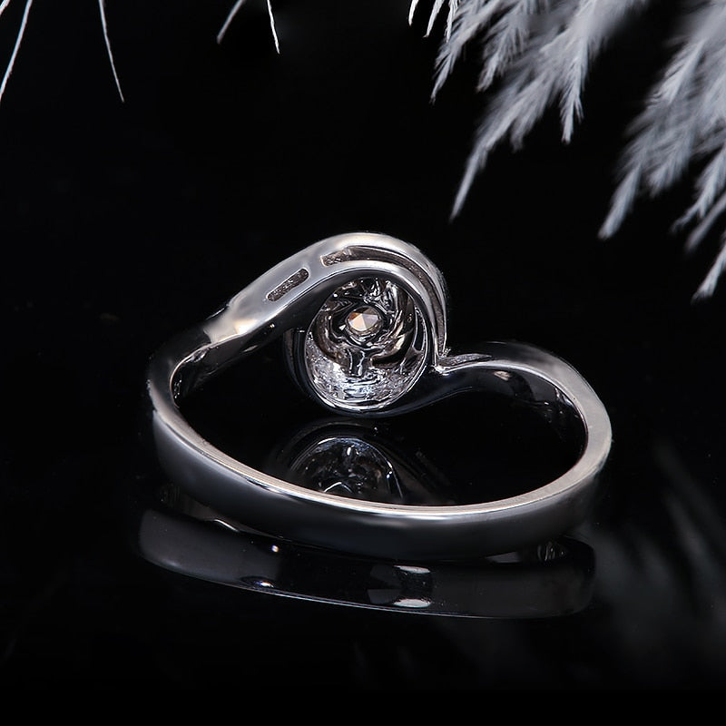 A silver round cut engagement ring set with a round moissanite on a pave bypass shank reminiscent of a wave.