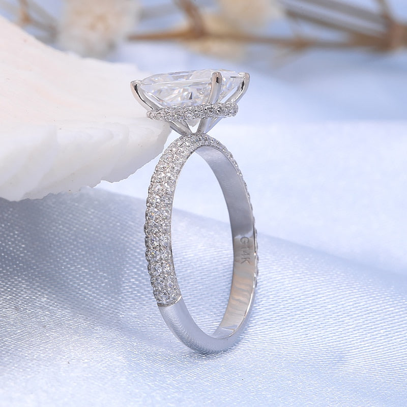 A silver ring featuring a 2CT radiant cut moissanite set in a hidden halo on a half gem encrusted band.