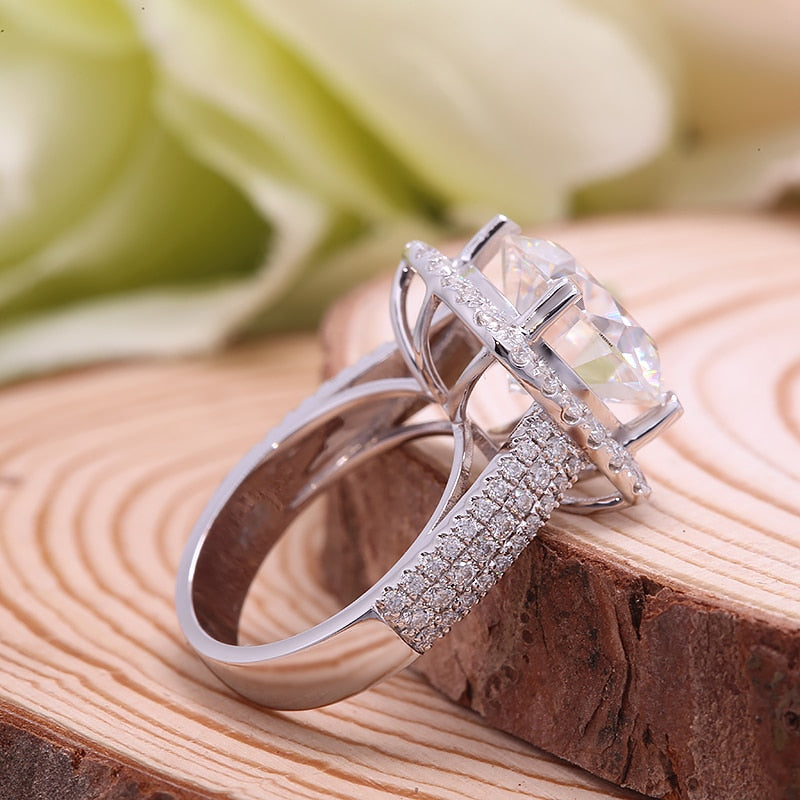A silver halo ring set with a 8CT round moissanite in a wide half pave band.
