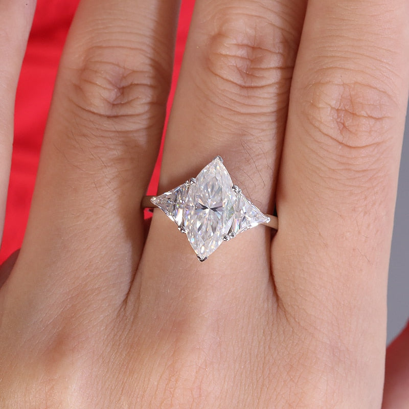 A hand wearing a silver 3 stone ring set with a 3CT marquise moissanite and with a 1.2CT trillion cut moissanite on each side.