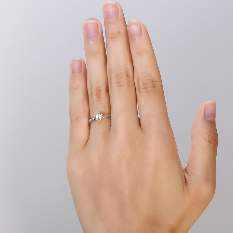 A hand wearing a silver small round solitaire with a tapered band.