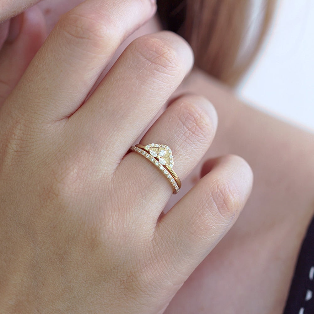 A hand wearing a gold crown engagement ring set with 3 small marquise cut moissanites and lined in small round moissanites accompanied by a matching wedding ring.