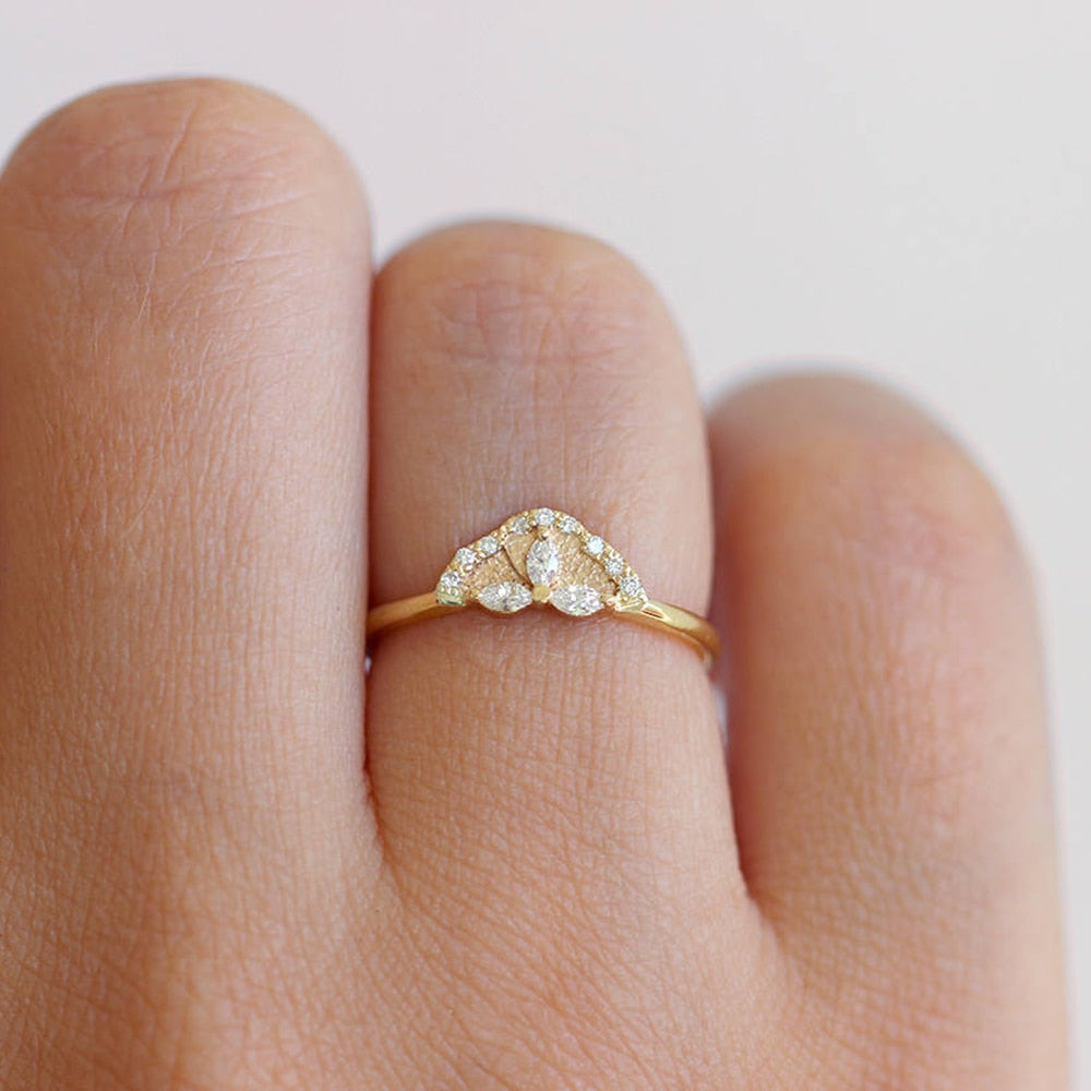 A hand wearing a gold crown engagement ring set with 3 small marquise cut moissanites and lined in small round moissanites.