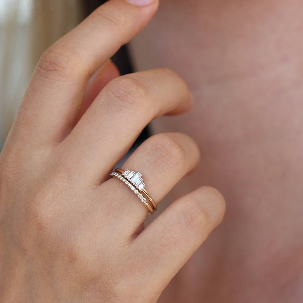 A hand wearing a gold ring set with 5 varying sized emerald cut moissanites that create a chevron shape.