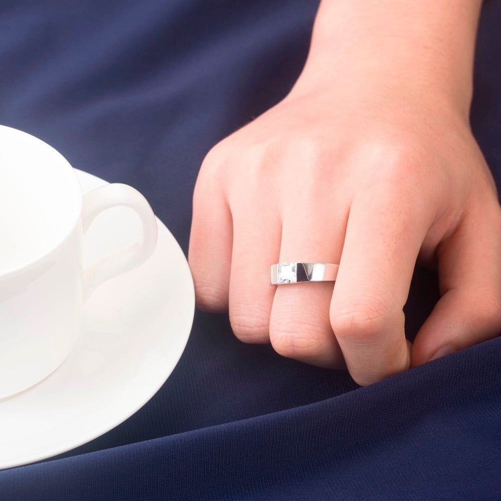 A hand wearing a silver thick band tension set with a round cut moissanite.