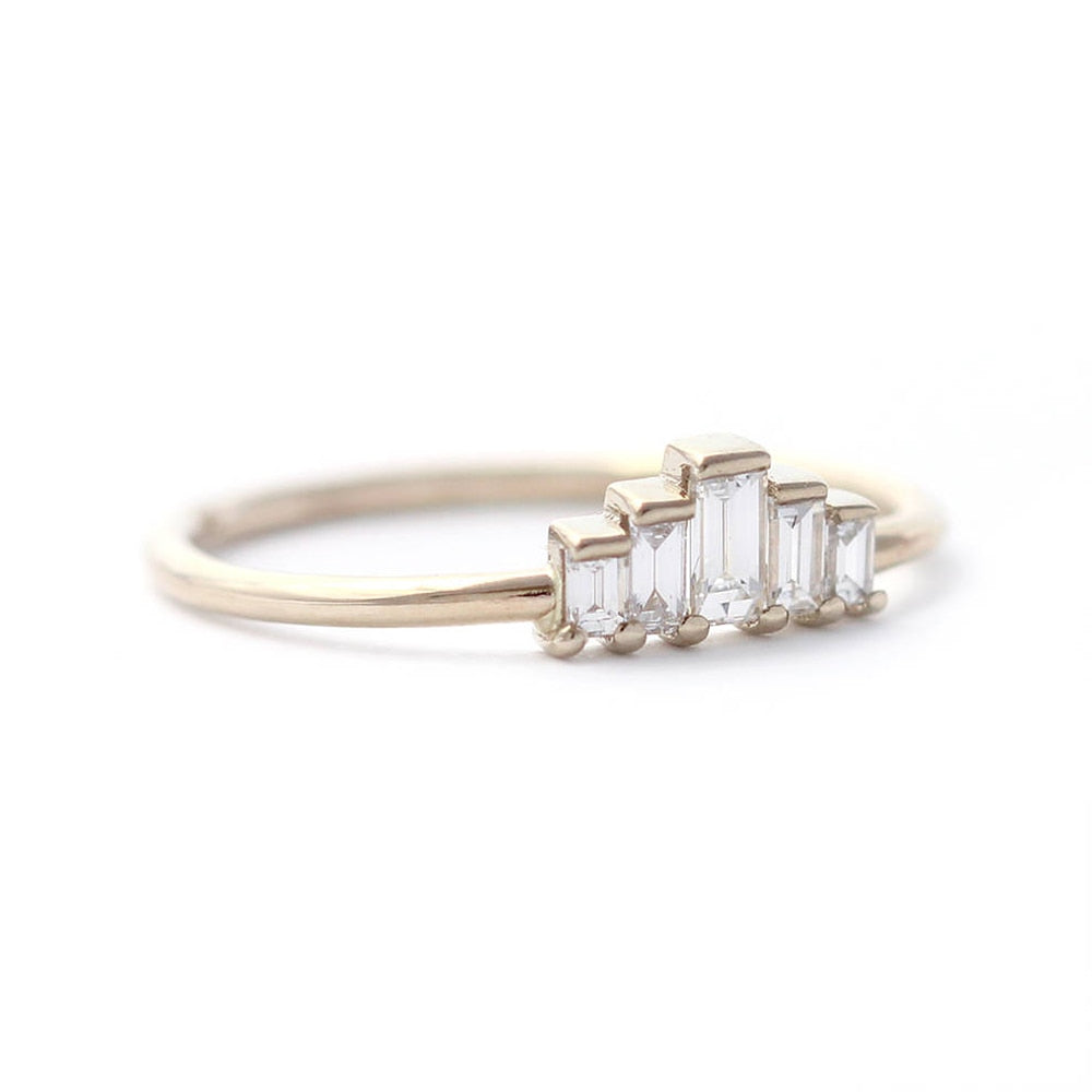 A gold ring set with 5 varying sized emerald cut moissanites that create a chevron shape.