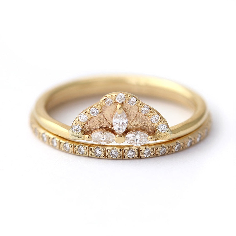 A gold crown engagement ring set with 3 small marquise cut moissanites and lined in small round moissanites accompanied by a matching wedding ring.