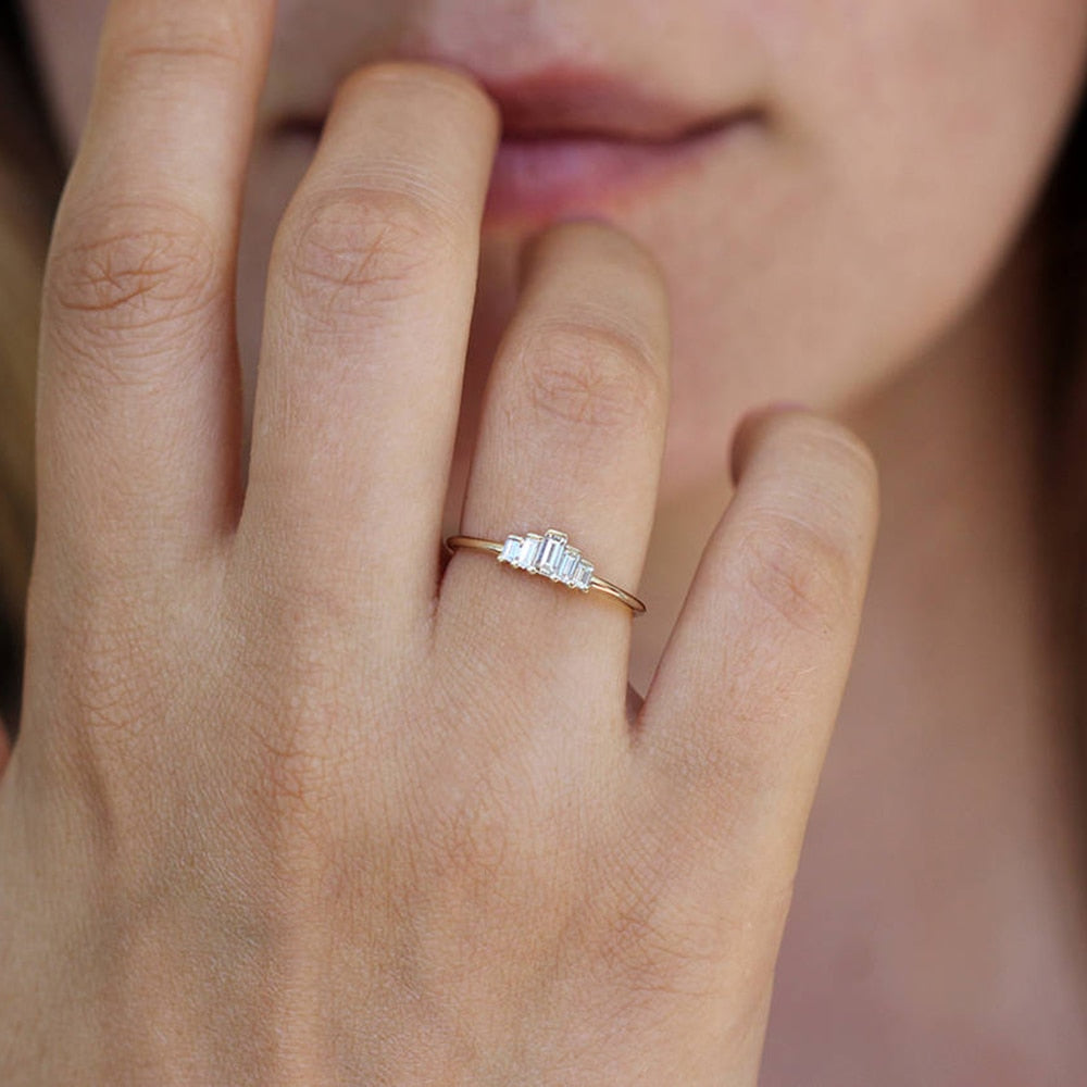 A hand wearing a gold ring set with 5 varying sized emerald cut moissanites that create a chevron shape.