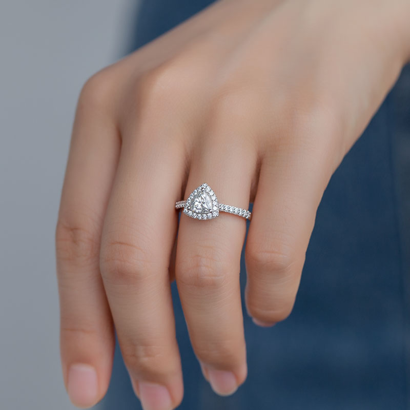 A hand wearing a silver trillion cut halo engagement ring with pave band.