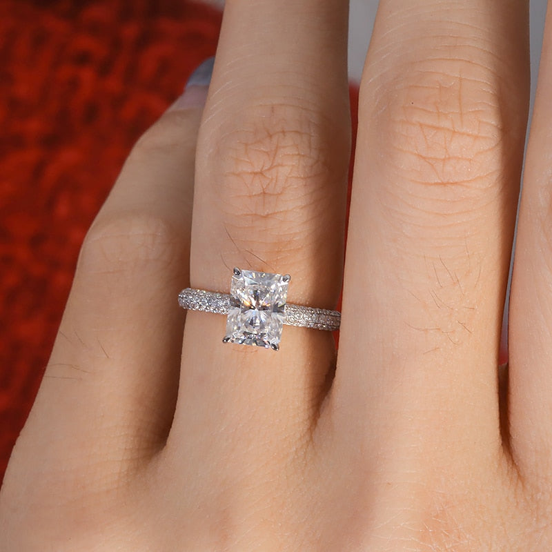 Hand wearing a silver ring featuring a 2CT radiant cut moissanite set in a hidden halo on a half gem encrusted band.