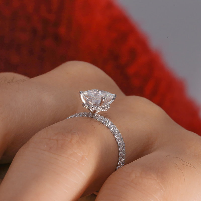 Hand wearing a silver ring featuring a 2CT radiant cut moissanite set in a hidden halo on a half gem encrusted band.